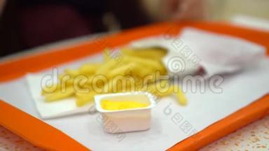 那个女孩在商场的一张小桌子后面吃薯条。 美食广场上漂亮迷人的女孩。 快餐