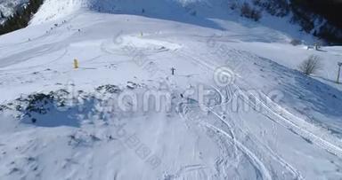 空中跟随滑雪者高山滑雪，狗在冬天的雪山滑雪场后面在阳光明媚的日子里奔跑