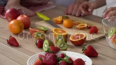 父母和儿子一起做水果沙拉。 明亮的水果多汁。 水果甜水果沙拉.. 准备健康的食物。