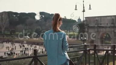游客深色头发的女人在意大利罗马用智能手机拍摄君士坦丁拱门和竞技场的照片。 慢动作。