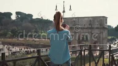 年轻女子在一个阳光明媚的日子里，用她的智能手机在意大利罗马拍摄君士坦丁拱门的照片。 慢动作。