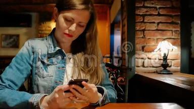 穿着棉袄在咖啡馆里用智能手机的漂亮女孩。 <strong>复古</strong>的内饰。 <strong>砖墙</strong>。