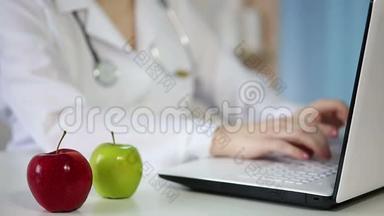 女医生在笔记本电脑键盘上打字，吃着苹果。 健康的生活方式