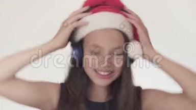 戴着圣诞老人帽子的美丽顽皮的少女在耳机上听音乐，在白色背景上唱歌