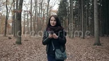美丽的年轻的布鲁内特女士使用智能<strong>手机</strong>在秋<strong>季</strong>公园。 秋天在森林里散步的女孩的生活方式概念