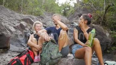 一群年轻的游客笑着休息在瀑布旁。 高清慢速运动。 泰国。