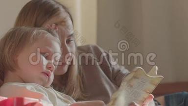 一位微笑的年轻可爱的母女在床上躺着看书放松的画像