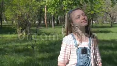 一个女孩带着耳机在公园里散步。 一个十几岁的女孩在户外听音乐。 一个少年在阳光明媚的阳光下带着手机走路