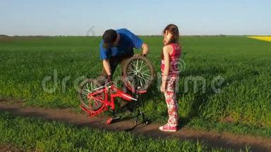一个带着孩子的人正在修理自行车。 爸爸和一个女儿在大自然中骑自行车。 那个人正在修理自行车