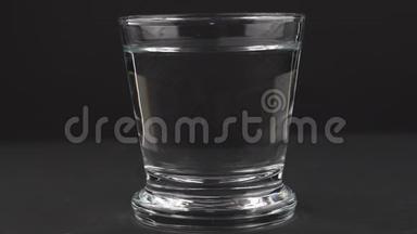 一片泡腾的止痛片落入玻璃杯中，在黑色背景下溶解慢镜头的阿司匹林