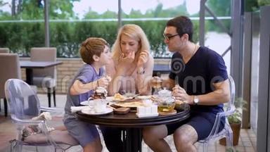 快乐的父母和小男孩坐在咖啡馆的露台上吃饭