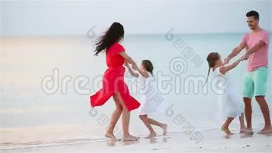 <strong>暑假</strong>期间在海滩上快乐的美丽家庭。 四口之家在海滩日落时玩得开心