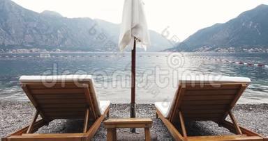两张带太阳伞的躺椅在被群山环绕的海边，€“避暑山庄浪漫度假”