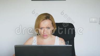 一个女人用她的笔记本电脑，坐在桌子旁，愤怒和愤怒，发誓。 人类的情感。 网络成瘾的概念。