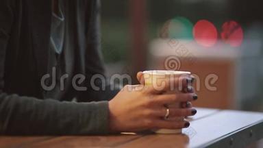 特写女人的手拿着一杯咖啡，从茶杯里冒出<strong>油烟</strong>。 模糊的灯光，城市街道