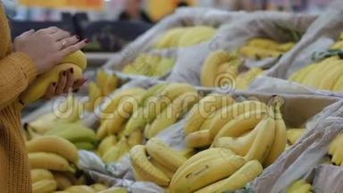 特写镜头看到年轻女子的手在<strong>超市</strong>里挑选香蕉，拿着一些。 展示<strong>水果</strong>。 4K