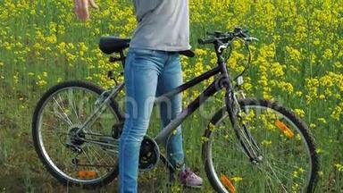 油菜田。 带着自行车的女孩在田野里开着黄色的花。 骑自行车的女孩正把胳膊伸过自行车