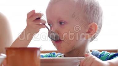 宝宝2岁用勺子吃粥.. 妈妈坐在男孩旁边。 家用家具