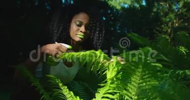 绿色构图。 这位美丽的美国黑人妇女，涂着绿色的口红和眼影，正在照顾这种蕨类植物。 她是