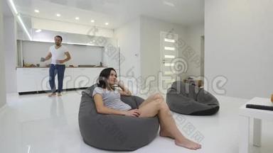 年轻女子在客厅里看电视，丈夫带咖啡来