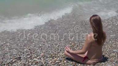 美丽的年轻女孩坐在海滩上的莲花姿势。 4K