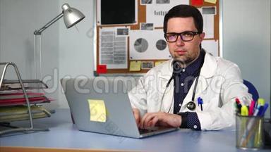 穿着白色外套的医生坐在柜子里，在他的笔记本电脑上工作。