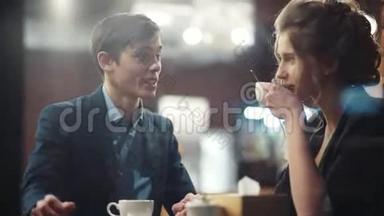 年轻的幸福夫妇交谈，喝咖啡，笑着约会。 他在智能手机上显示照片