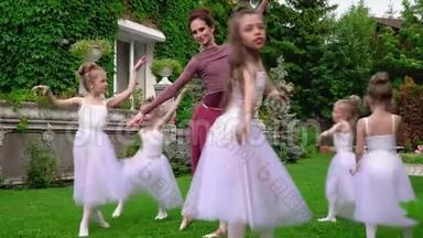 老师和小女孩一起在芭蕾舞学校的花园里跳芭蕾。 芭蕾舞演员在草坪上跳舞