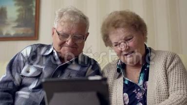 高级夫妻在沙发上使用电子标签。 一对快乐的老夫妇在数码平板电脑上视频聊天。
