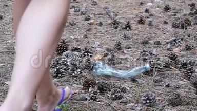 松林中的塑料瓶。 女人用脚咬塑料瓶。 慢动作