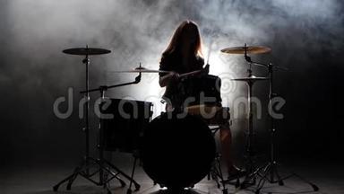 女孩是踢鼓，演奏精力充沛的音乐。 <strong>黑烟</strong>背景。 剪影