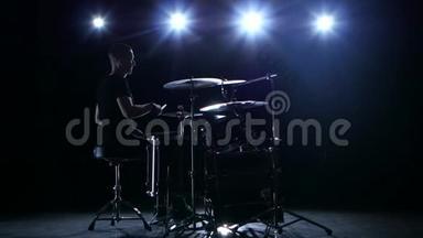 鼓手在鼓上大力演奏旋律。 黑色背景。 背光。 剪影
