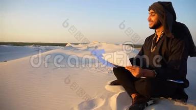 成功的阿联酋商人读<strong>商业计划书</strong>，夏天晚上坐在沙漠中的温暖的沙滩上