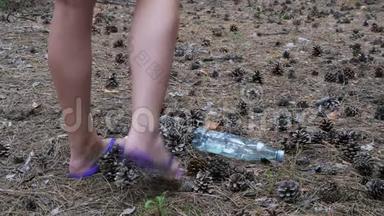 松林中的塑料瓶。 女人用脚踩着塑料瓶