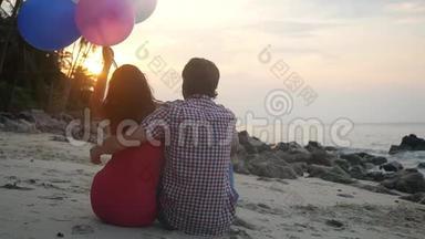 年轻夫妇坐在海滩上抱着气球看着日落。 慢动作。 1920x1080
