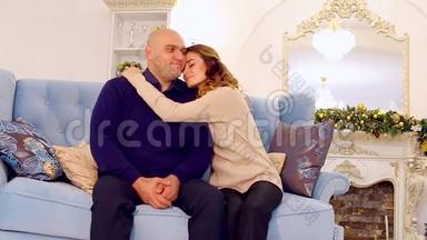 模范家庭、慈爱的父母和儿子的肖像，他们坐在节日装饰的房间里的蓝色沙发上，挂着圣诞树