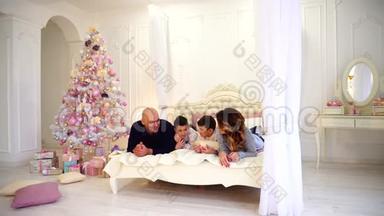 友好的家庭聊天躺在床上，爸爸妈妈和他们的孩子笑着，躺在明亮的卧室的大床上。