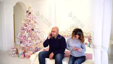 幸福的丈夫和妻子用智能手机祝贺亲戚的节日，坐在卧室的床上庆祝节日