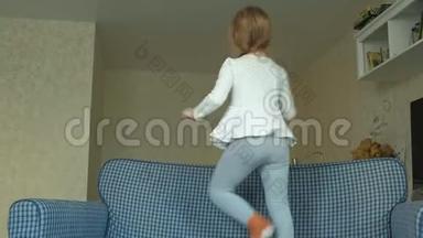 小女孩手里拿着手机，耳机跳着，在房间的沙发上跳舞