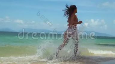穿着比基尼的年轻苗条的女士穿着奇异的白色沙滩，穿过大海，在阳光下泼水