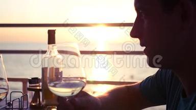 年轻有魅力的男人正在一家咖啡馆里，在大海和日落的背景下，喝着一杯葡萄酒。 高清高清