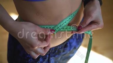 健身女运动员在锻炼后用胶带测量身体大小的特写镜头。 减肥的概念