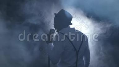 男歌手的视线从后面的烟雾和白光唱成麦克风和舞蹈。 黑色背景
