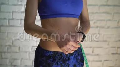 健身女运动员在锻炼后用胶带测量身体大小的特写镜头。 减肥的概念