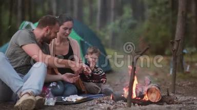 家庭在大自然中休息。 夫妻和他们的小儿子正在明火上煮棉花糖，吃它们。