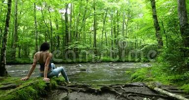 女徒步旅行者坐在深林瀑布附近。