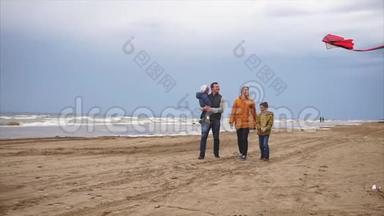 一个年轻的家庭在<strong>寒冷</strong>的<strong>天气</strong>里带着风筝沿着海滩散步