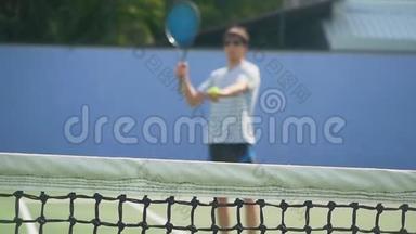 阳光明媚的一天，年轻人戴着太阳镜玩网球拍。 网格前景模糊的慢运动