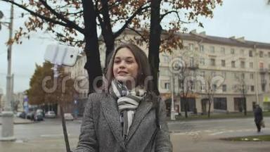 穿着外套的年轻漂亮女孩在城市的一条街道上自以为秋天。