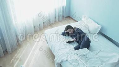 一个年轻可爱的女人，穿着睡衣，早上在床上看书。 在床上看书的漂亮年轻女子